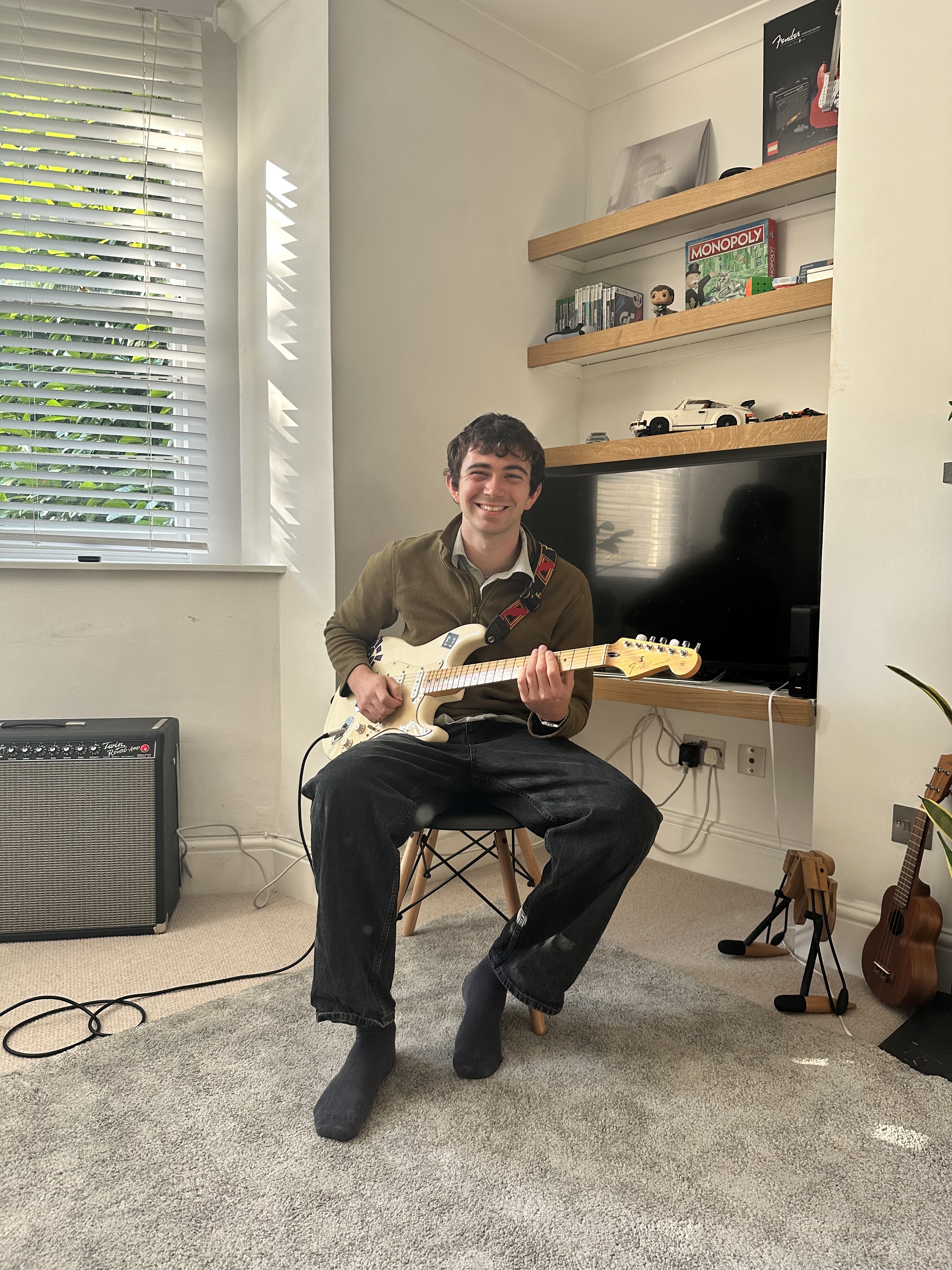 A man is playing a guitar, standing in front of an amplifier and another instrument. Image Description A young man sitting...